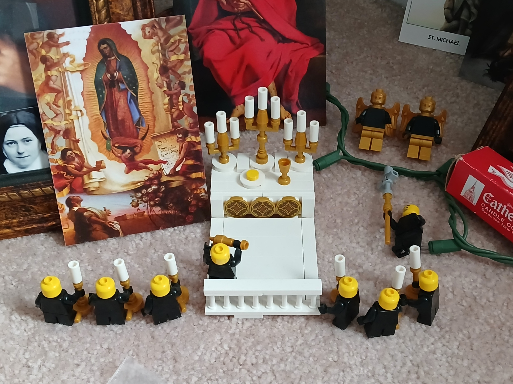 A brick-built altar with candles, chalice, and minifigures displayed beside an image of Our Lady of Guadalupe